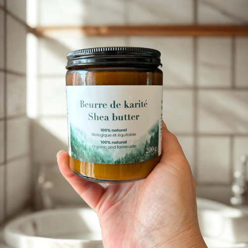 Pot de beurre de karité Eco Loco, 100 % naturel, biologique et équitable, tenu par une main et la personne se trouve dans une salle de bain blanche.
