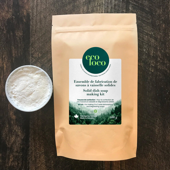Pochette en papier kraft avec le logo d'Eco Loco contenant un ensemble de fabrication de savons à vaisselle solides sur une comptoir de bois avec une contenant de savon cake vaisselle 