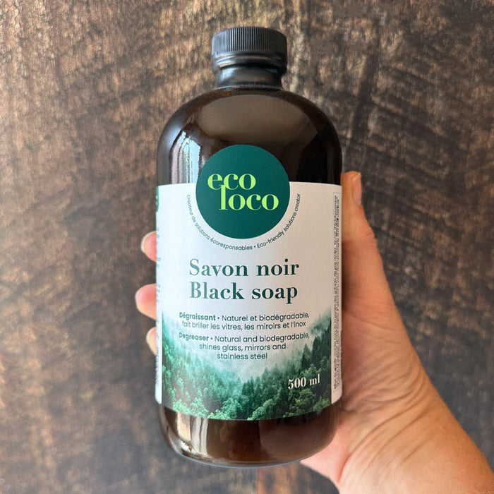 Bouteille de savon noir black soap tenue par une main et un fond en bois