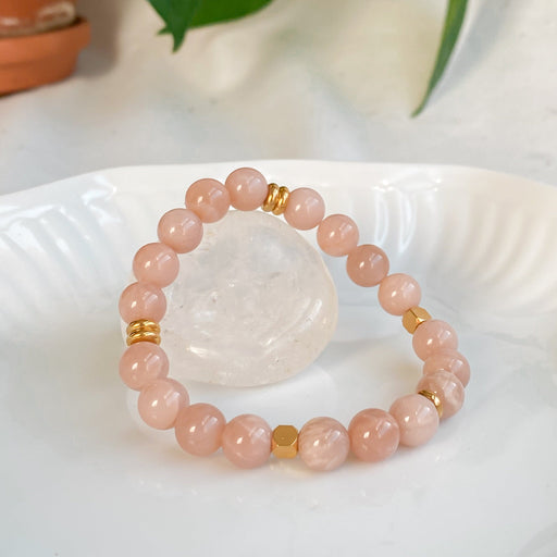 Bracelet Sparkles en pierre de soleil 8mm et acier inoxydable doré sous un autre angle, posé sur une pierre brute de quartz clair, avec une lumière naturelle et un décor végétal.