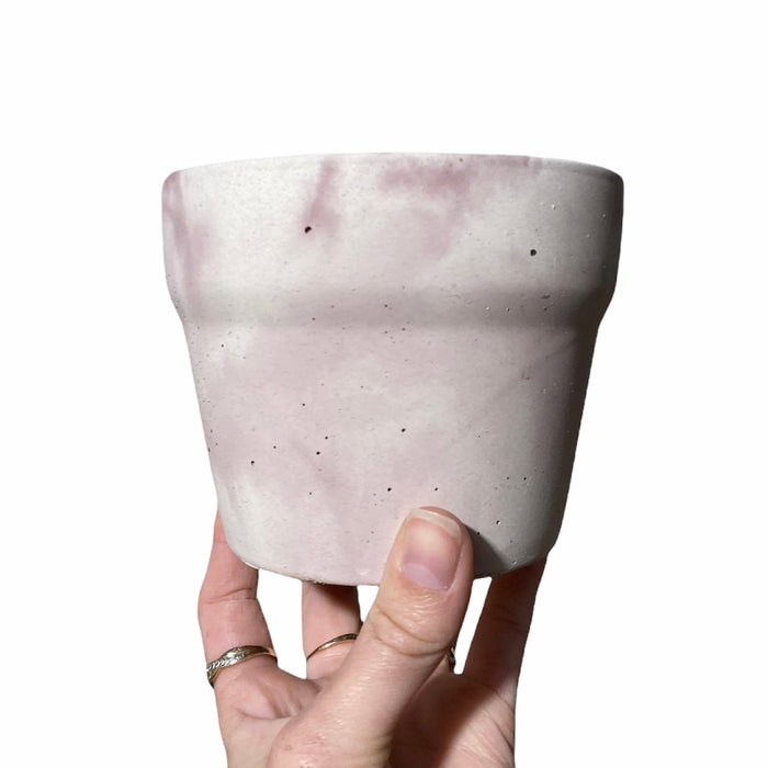 Pot de béton marbré rose et blanc tenue dans une main